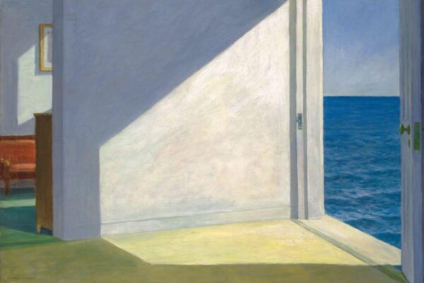 A sunlit room with an open doorway leading to a view of the blue ocean, casting strong geometric shadows across the interior floor and walls.
